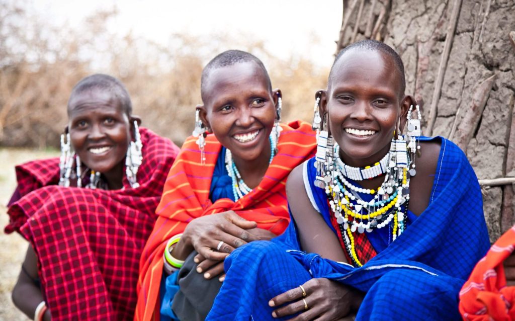 Three smiling Masai women in colorful garbs and festive jewelry