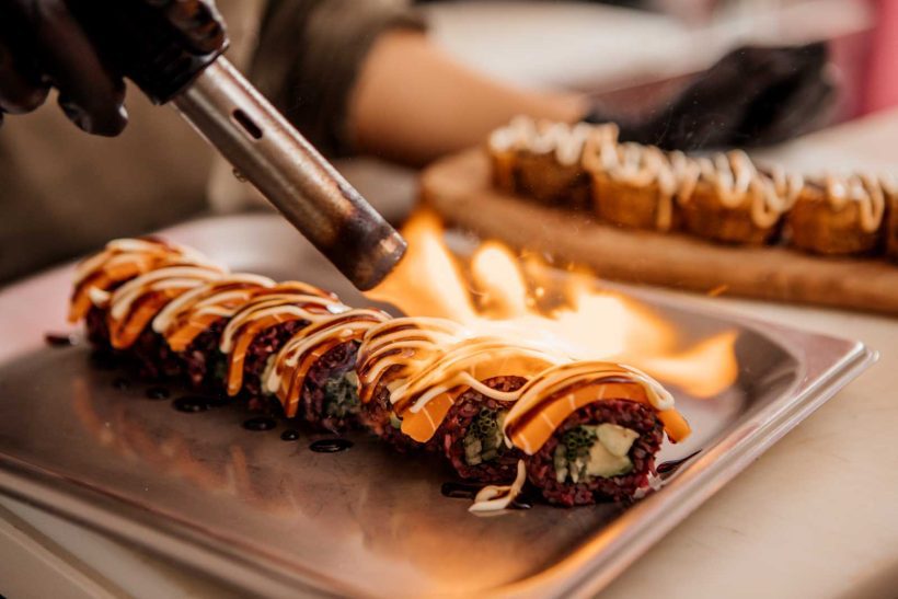 A close-up view of a blow torch blowing fire on a sushi roll.