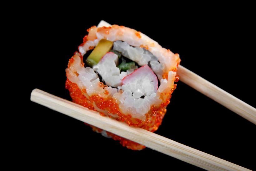 A close-up view of the California Roll, held between two chop sticks.
