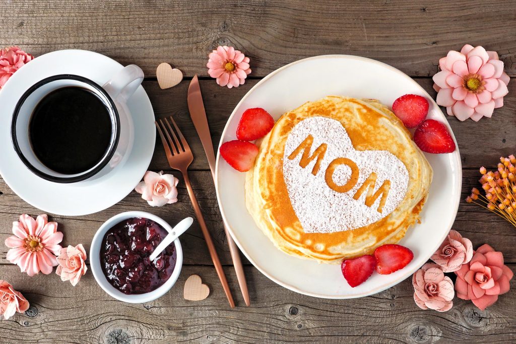 overhead shot of a Mother's Day breakfast with pancakes, coffee, chocolate spread, & mom's favorite flowers